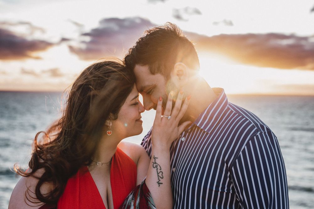 Romantic couple shares tender moment on beach during vibrant sunset by the sea.