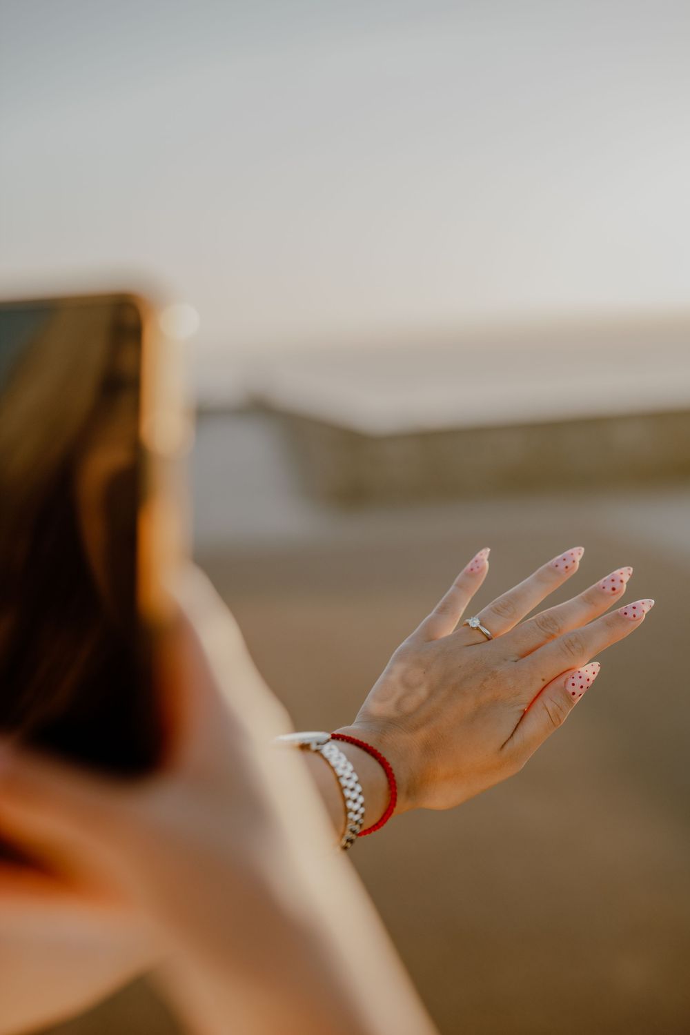 Close-up of woman's hand with manicured nails and bracelet against blurred sunset background.