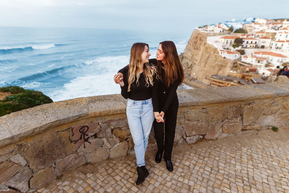 Couple walking along scenic coastal path with white buildings and ocean views in Portugal.