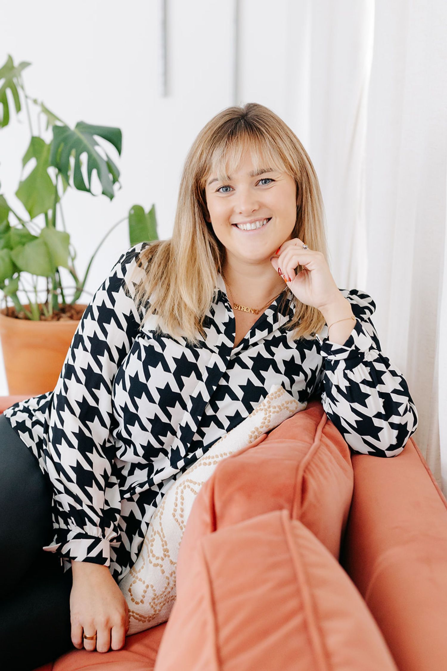 A series of photos showing someone in a black and white houndstooth top lounging on a coral-colored couch with plants in background.