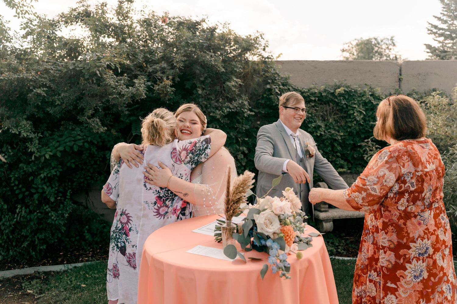 Wedding party shares drinks and laughter during an outdoor sunset celebration in a garden setting.