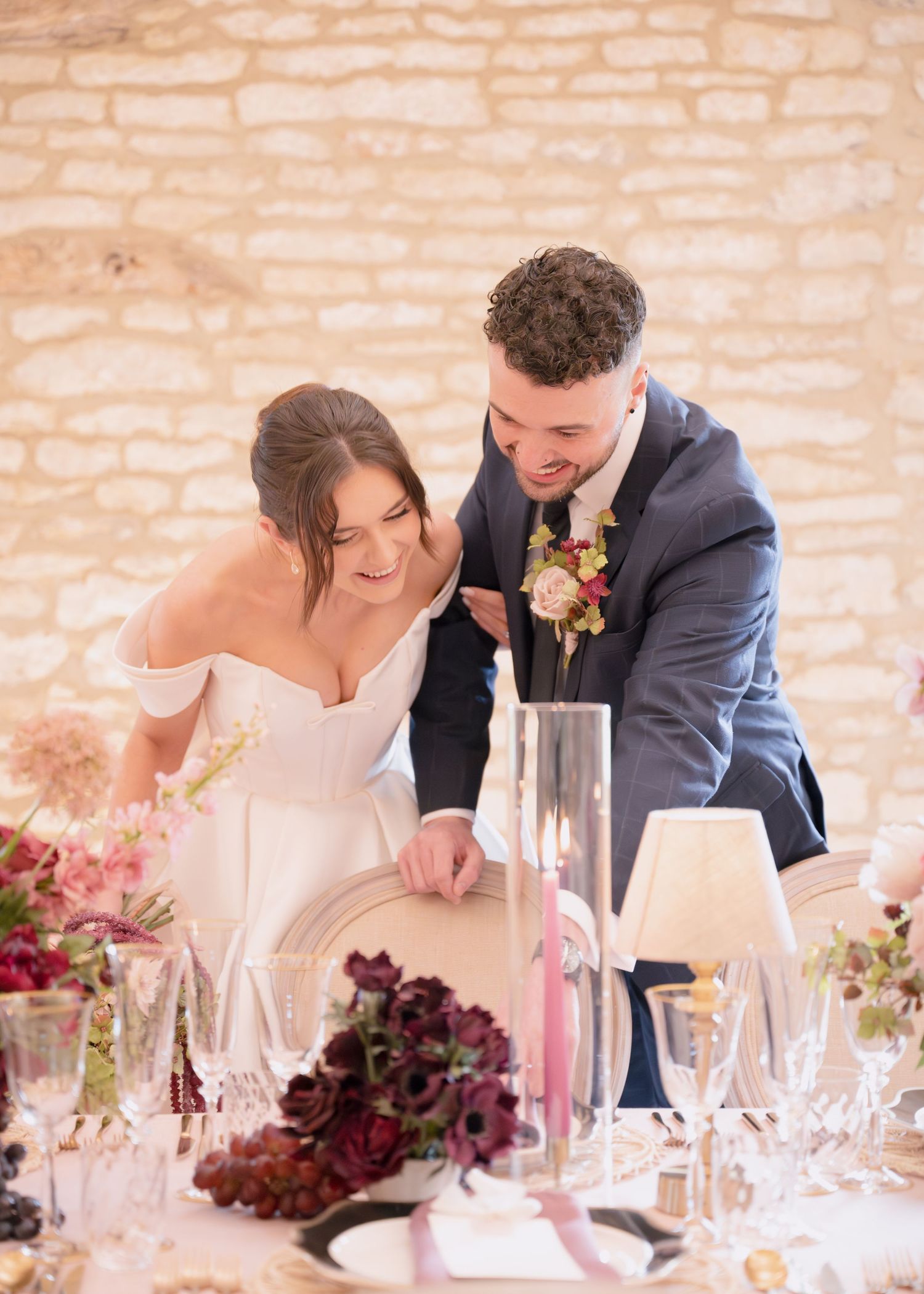 A happy bride and groom laugh together at an elegantly decorated wedding reception table indoors.