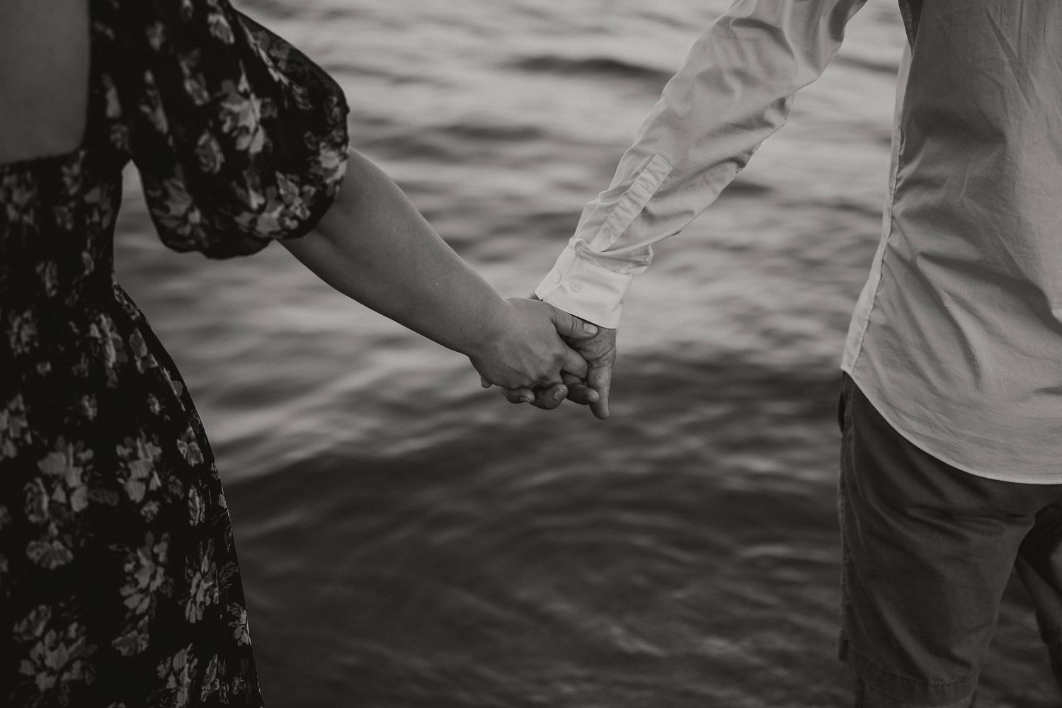 Couple holding hands while walking along the water's edge.