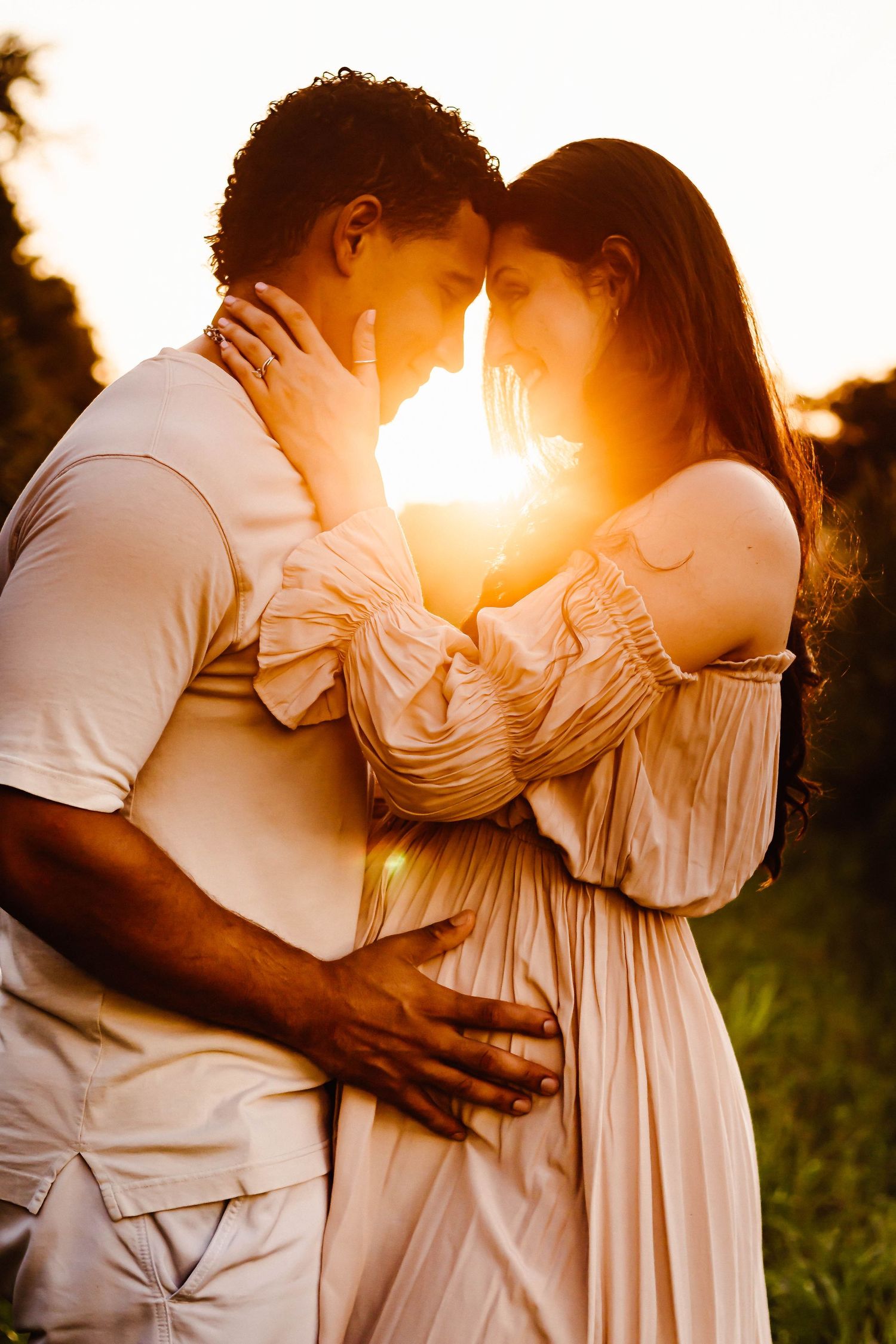 Couple embracing in warm sunset light wearing light colored clothing in a natural setting.