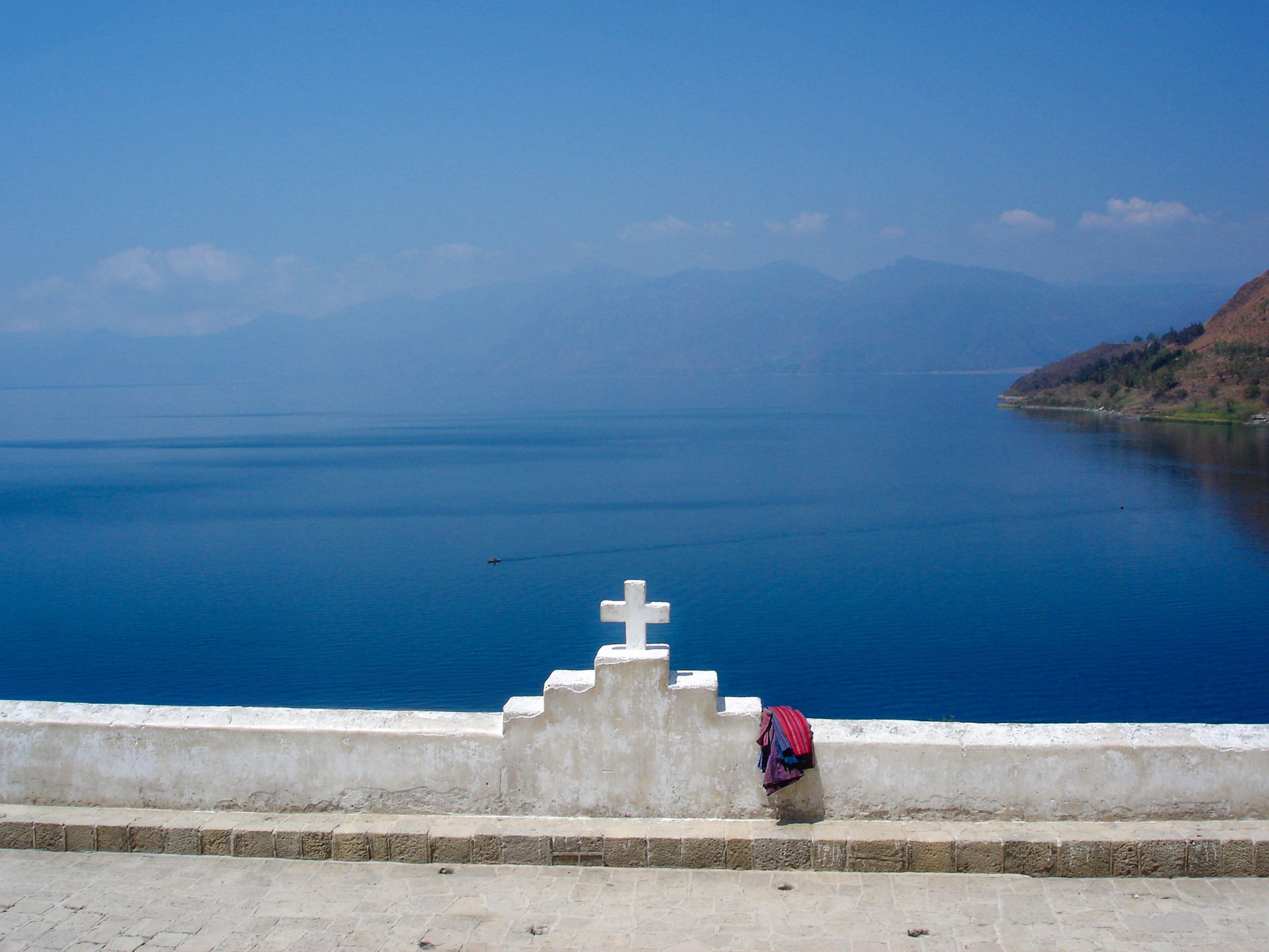 White cross monument overlooking deep blue water of Lake Atitlán in Guatemala.
