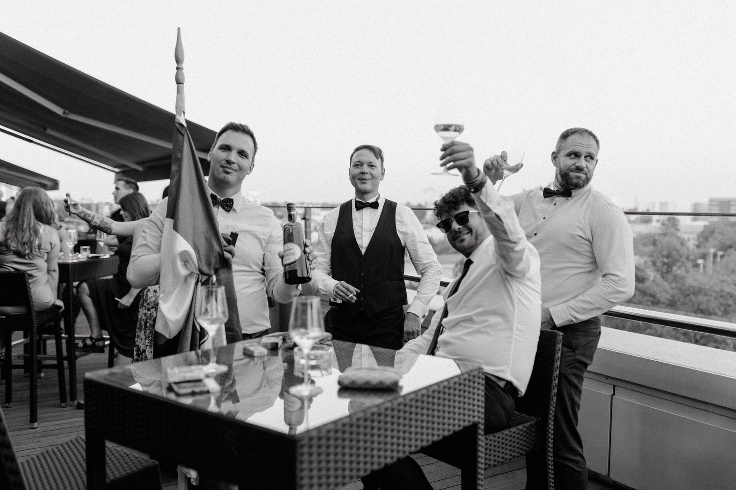 People enjoying drinks and socializing at a black and white outdoor rooftop bar celebration.