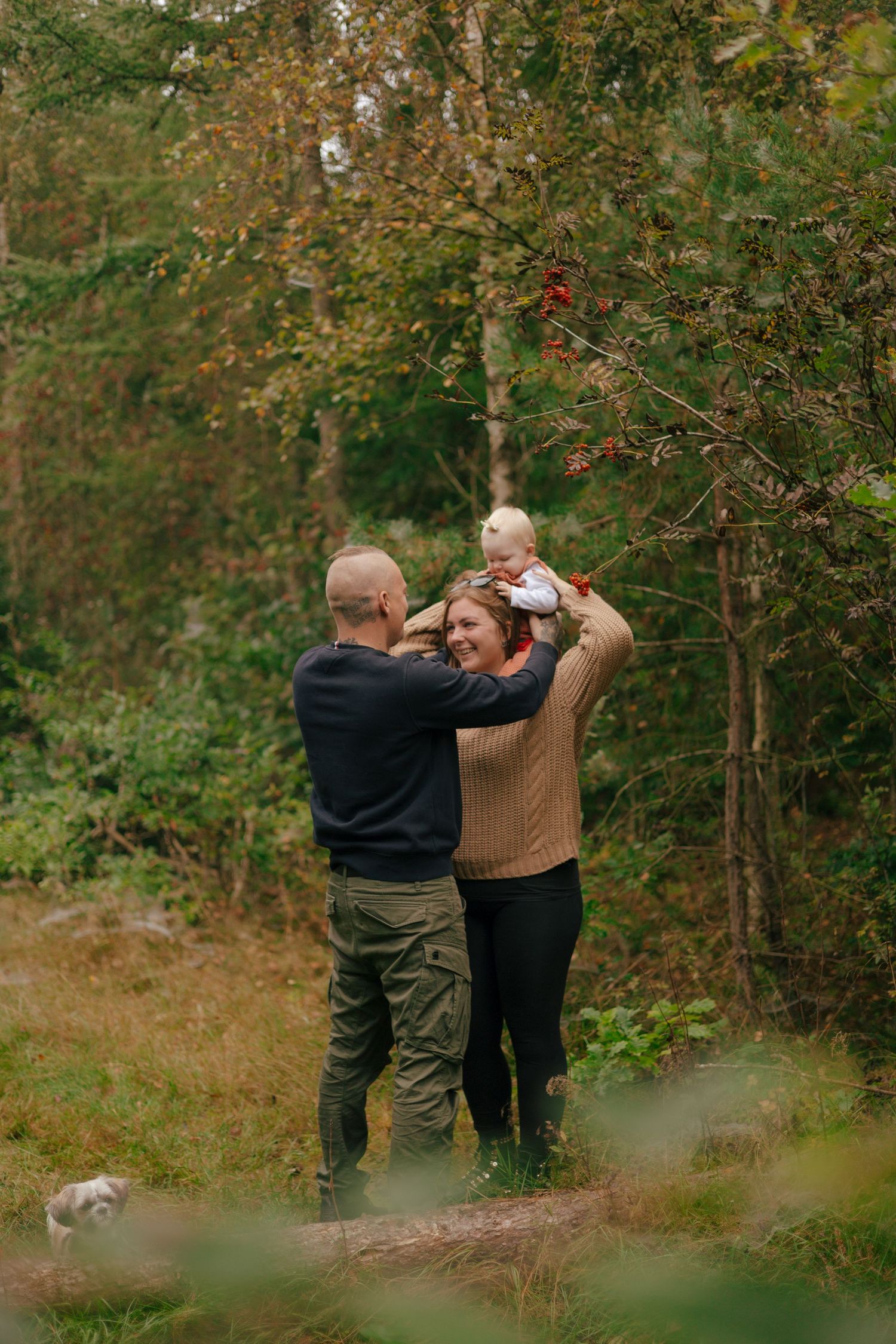 Couple playing with baby while standing in autumn woods.