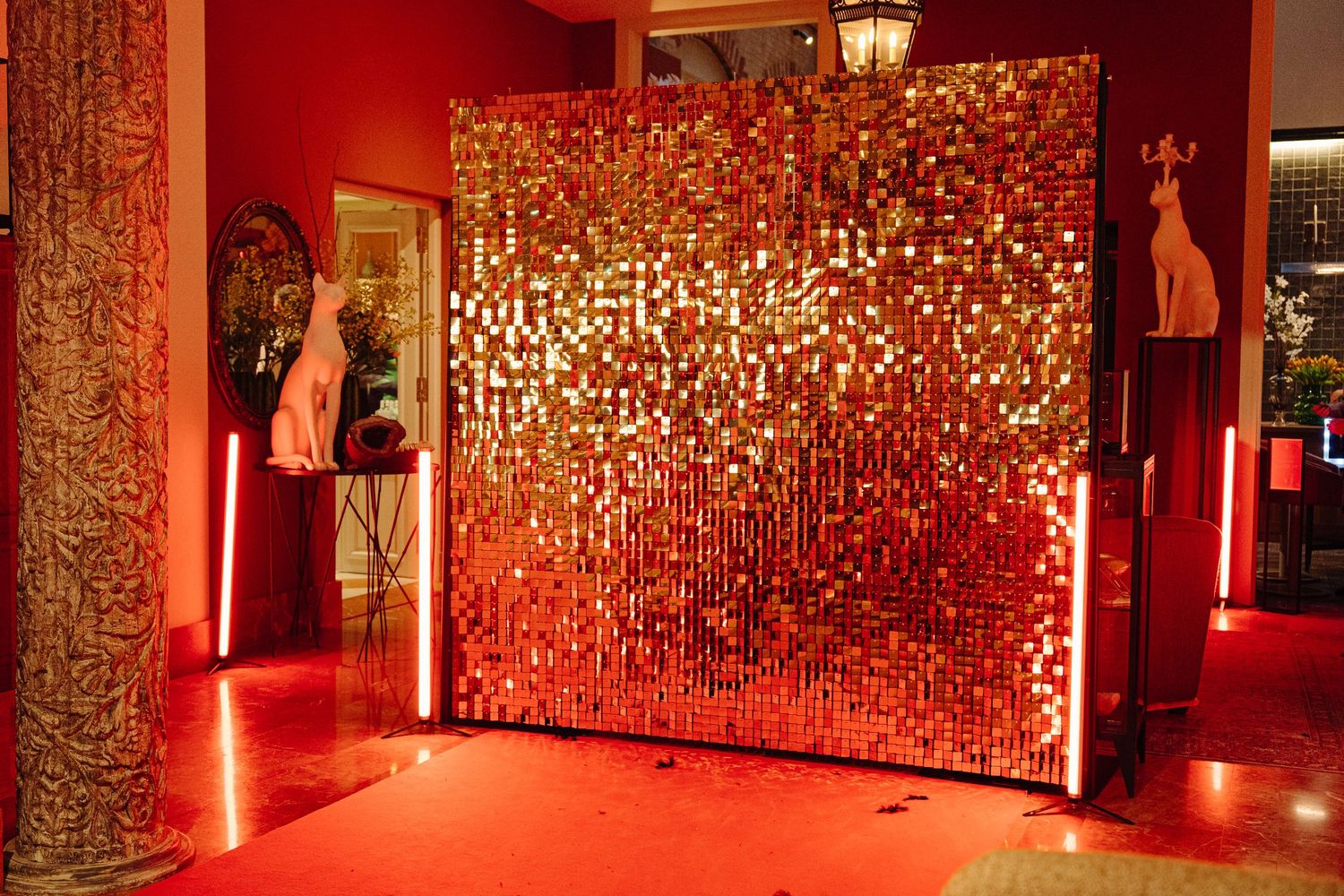 Glamorous gold sequin photo booth backdrop wall with red lighting in an elegant event venue.