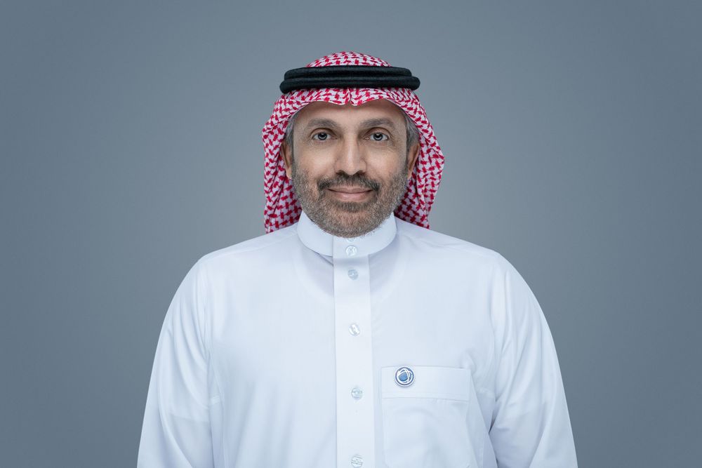 Person wearing traditional Middle Eastern white thobe and red and white checkered keffiyeh against gray background.