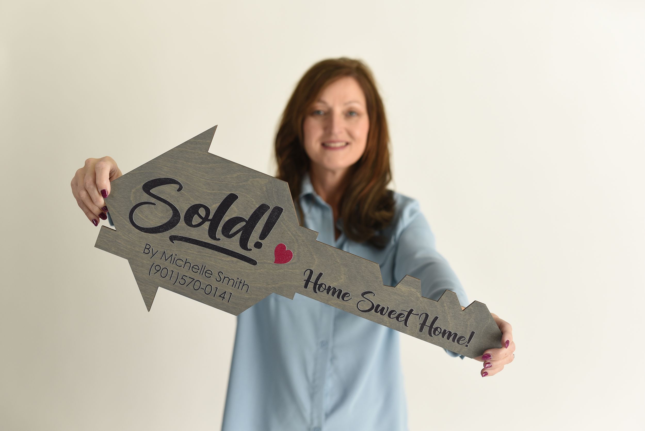 Real estate agent in light blue shirt holds up arrow-shaped 'Sold' sign against white background.