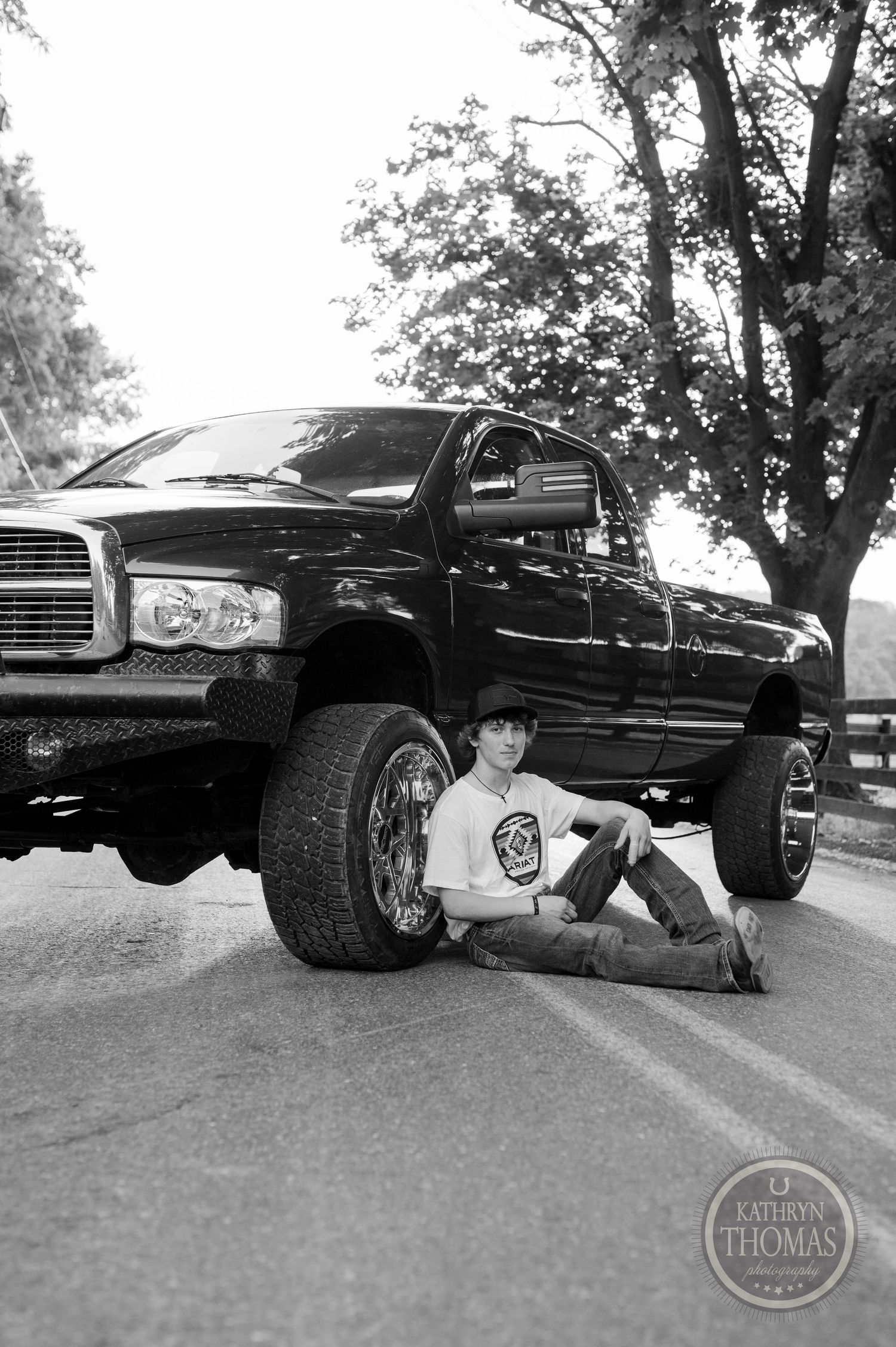 Black Dodge Ram pickup truck with lifted suspension and oversized tires parked on a rural road.