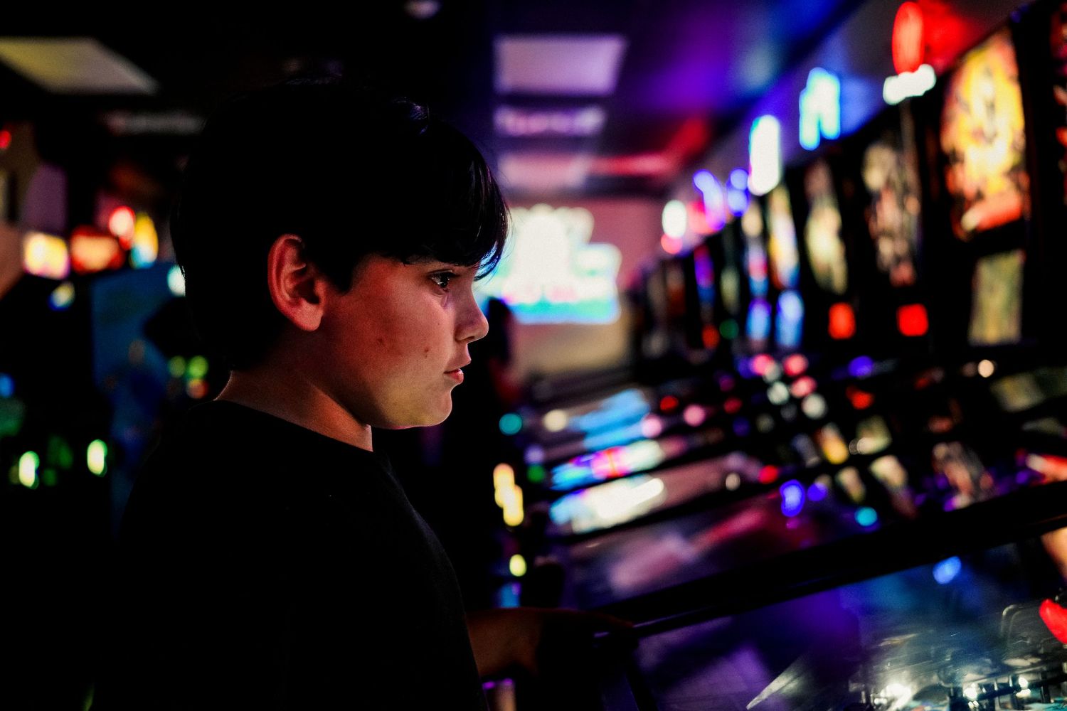 Dark silhouette in gaming arcade with colorful neon lights and slot machines glowing in the background.
