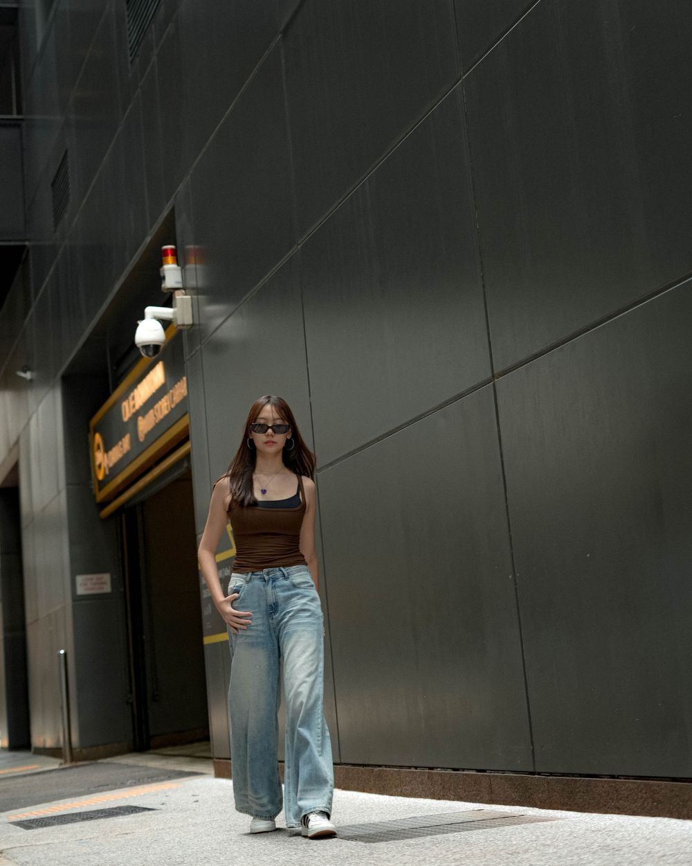 Street fashion portrait with wide-leg jeans and brown top against modern architecture.