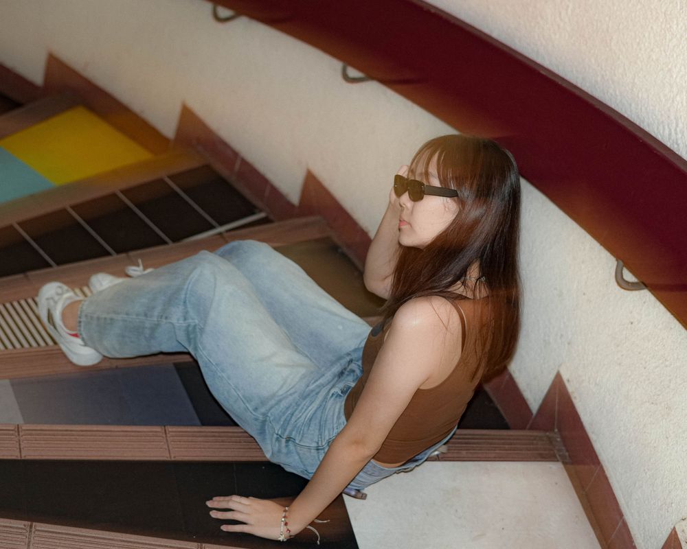 A casual pose on wooden stairs with sunglasses and retro-inspired outfit.
