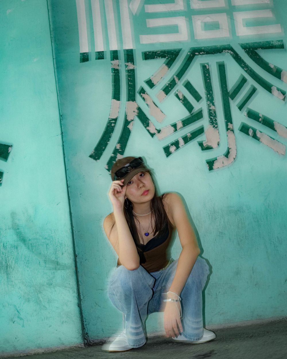 A crouching pose against turquoise wall with geometric patterns.