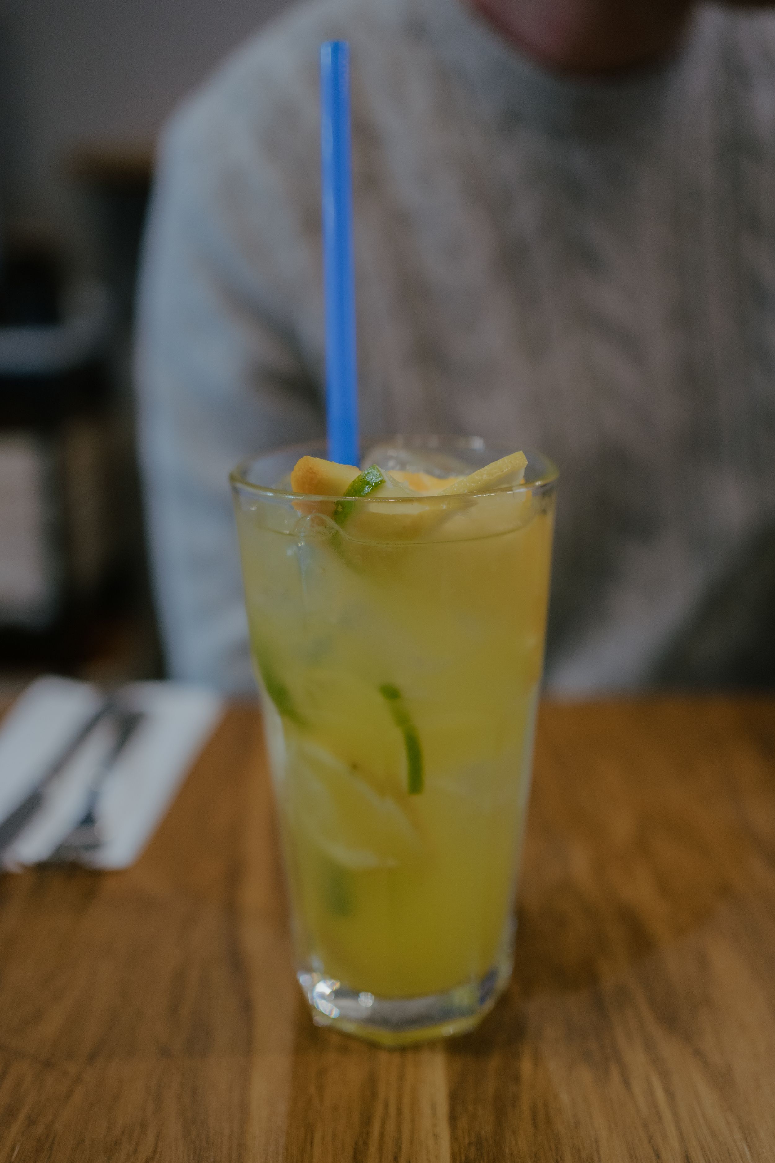 Tall glass of yellow citrus cocktail garnished with lime and orange slices on wooden table.