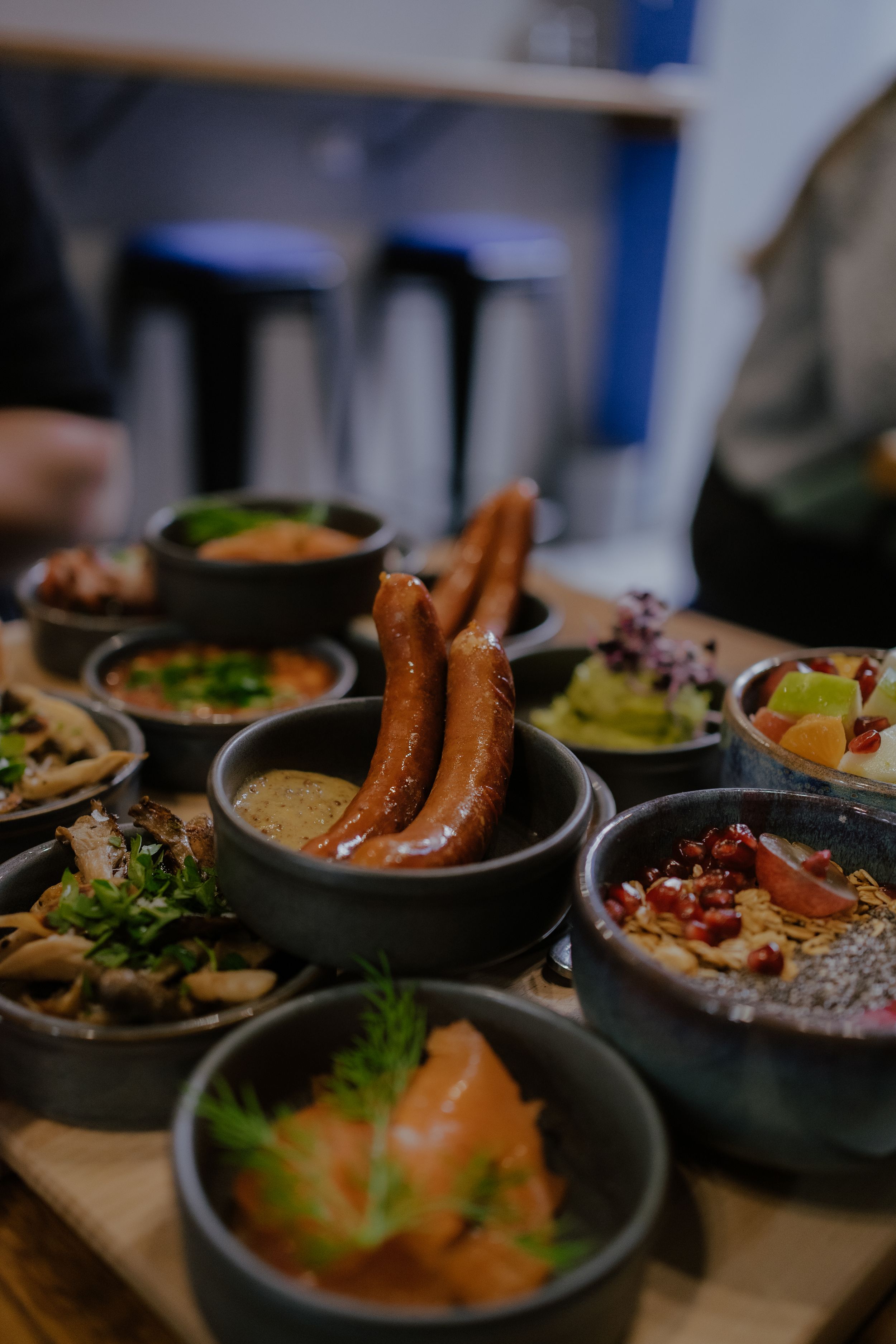 Variety of German dishes served in dark ceramic bowls including sausages, salmon, and salads on a wooden serving board.
