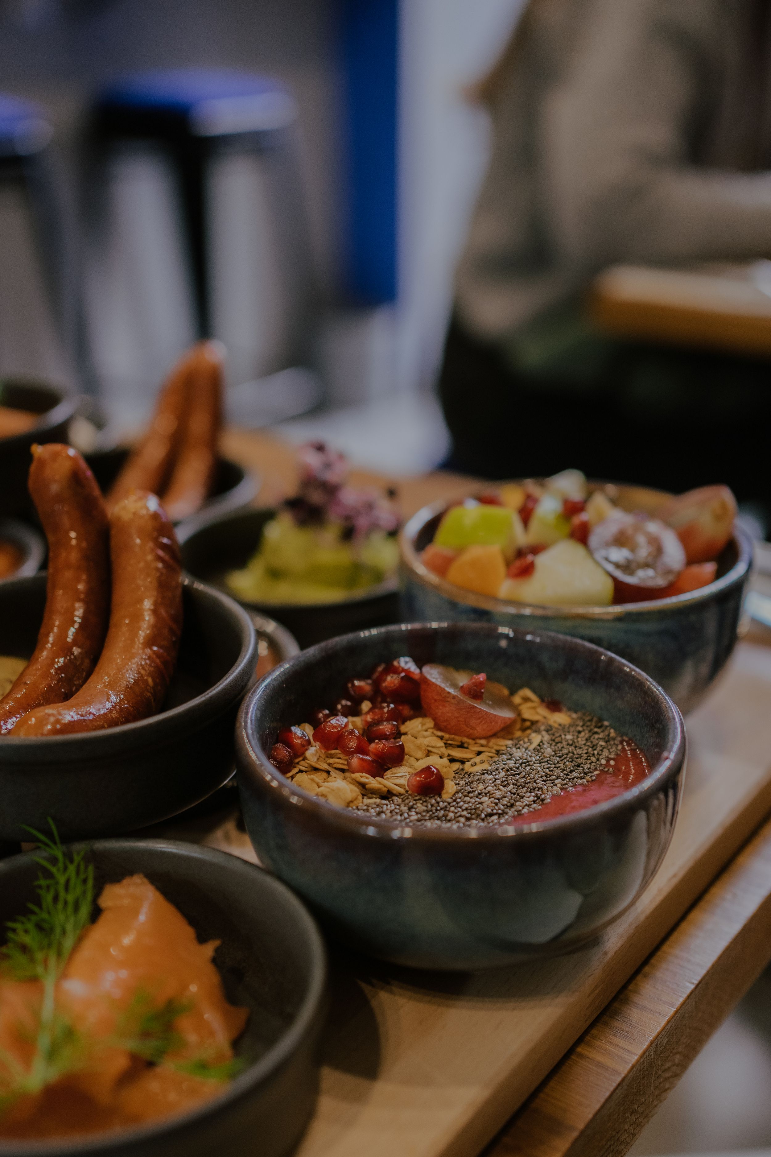 Close-up view of traditional German appetizers featuring bratwurst, salmon, and grain bowls arranged on wooden surface.