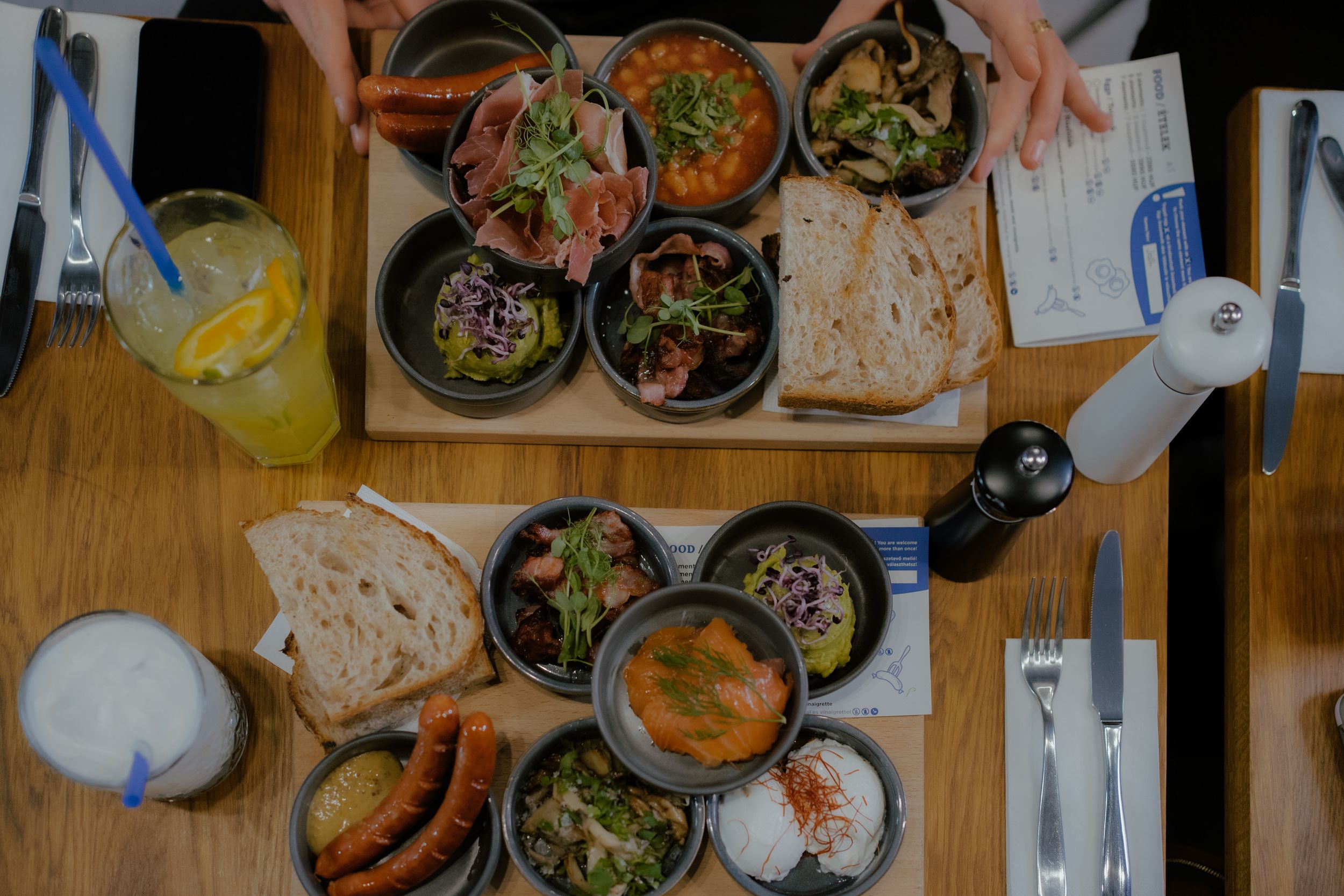 Overhead view of various dishes and bowls on a wooden table with bread and drinks during a casual dining setting.