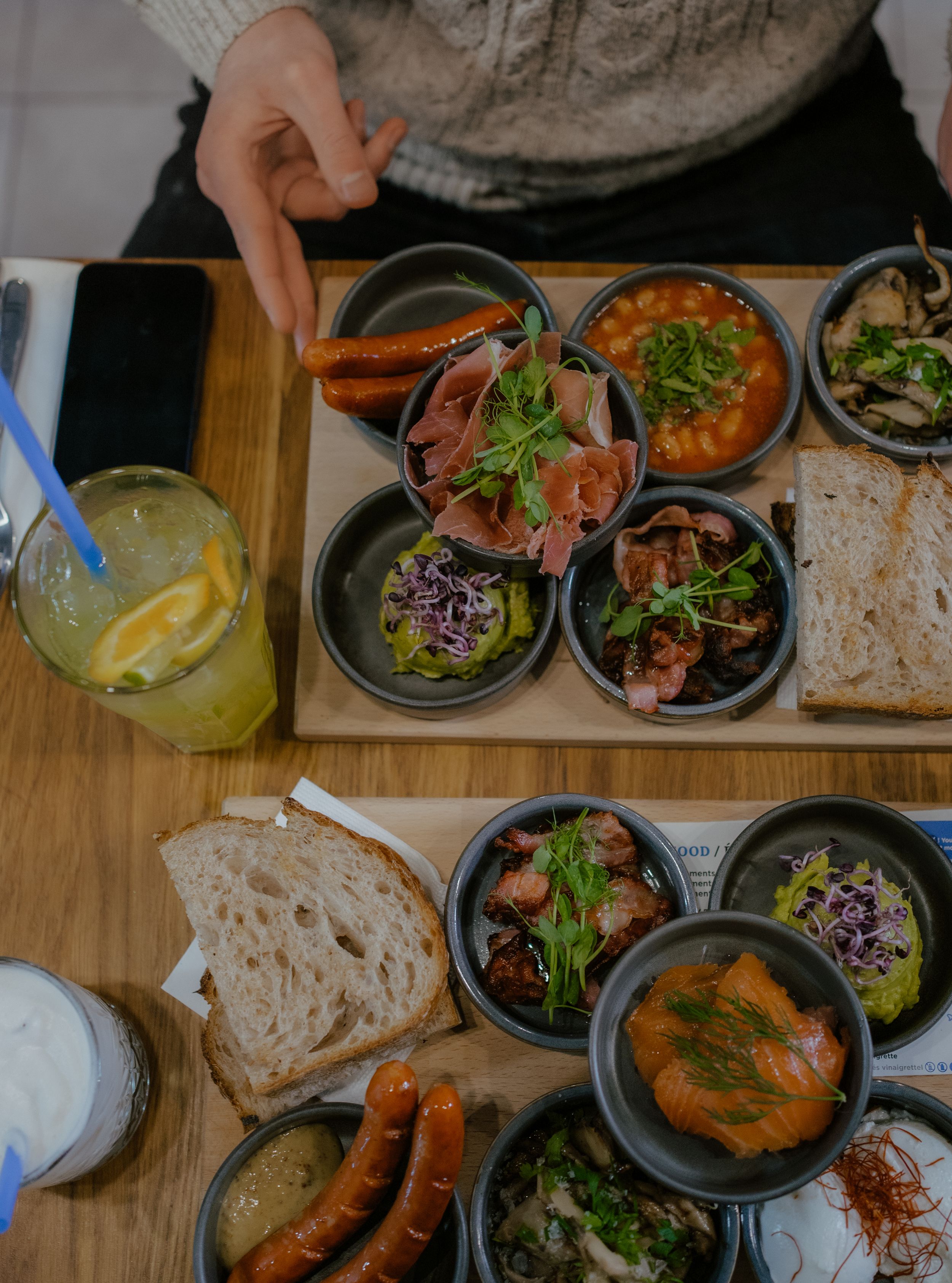Overhead view of various small dishes with appetizers, sauces, and bread served alongside a yellow citrus cocktail.