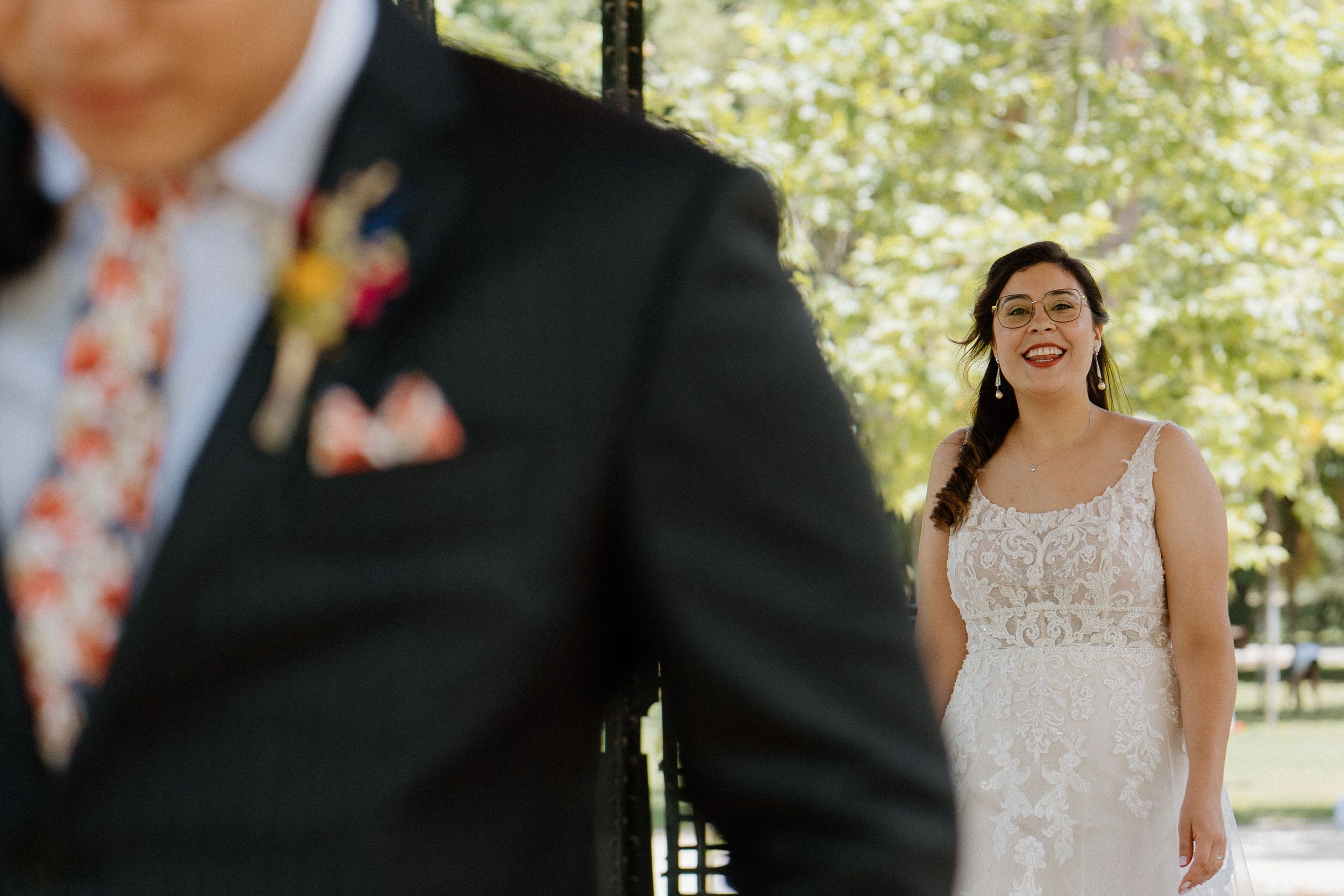 Someone in white lace wedding dress smiles joyfully during a first look moment in a sun-dappled garden.