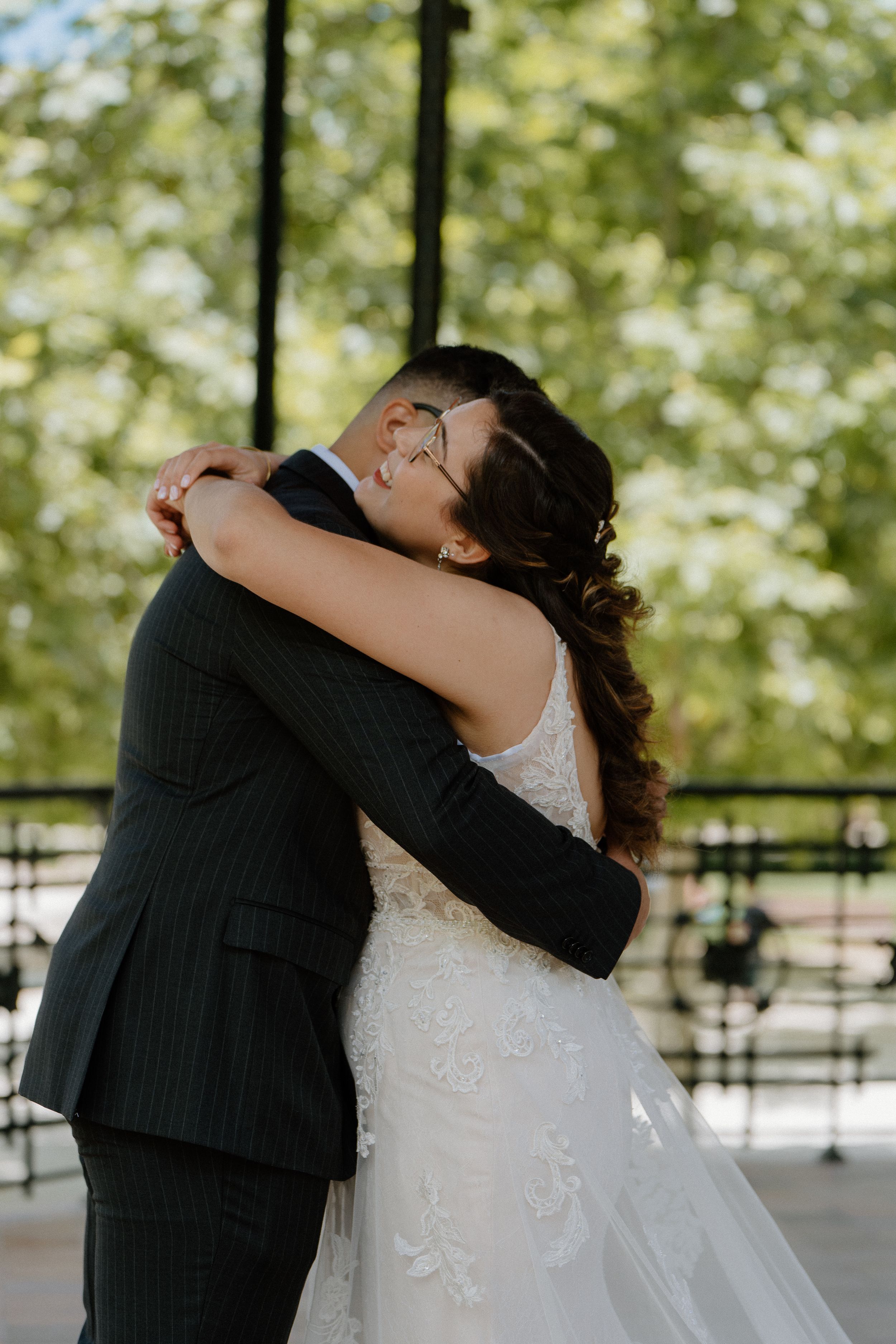 A couple embraces in a tender moment during their wedding, the bride wearing a white lace gown outdoors.