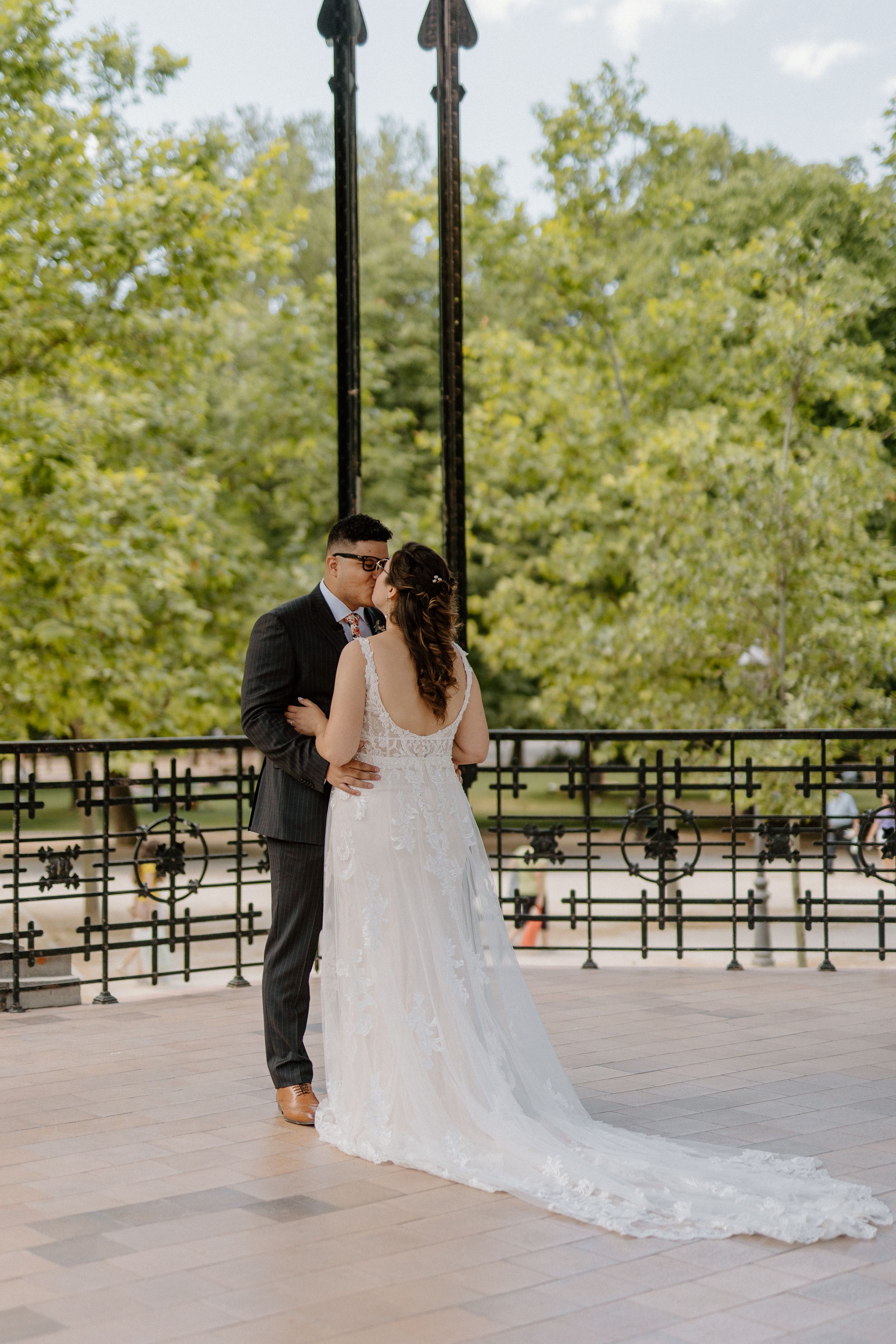A newlywed couple shares an intimate dance on a covered patio surrounded by greenery and ornate railings.