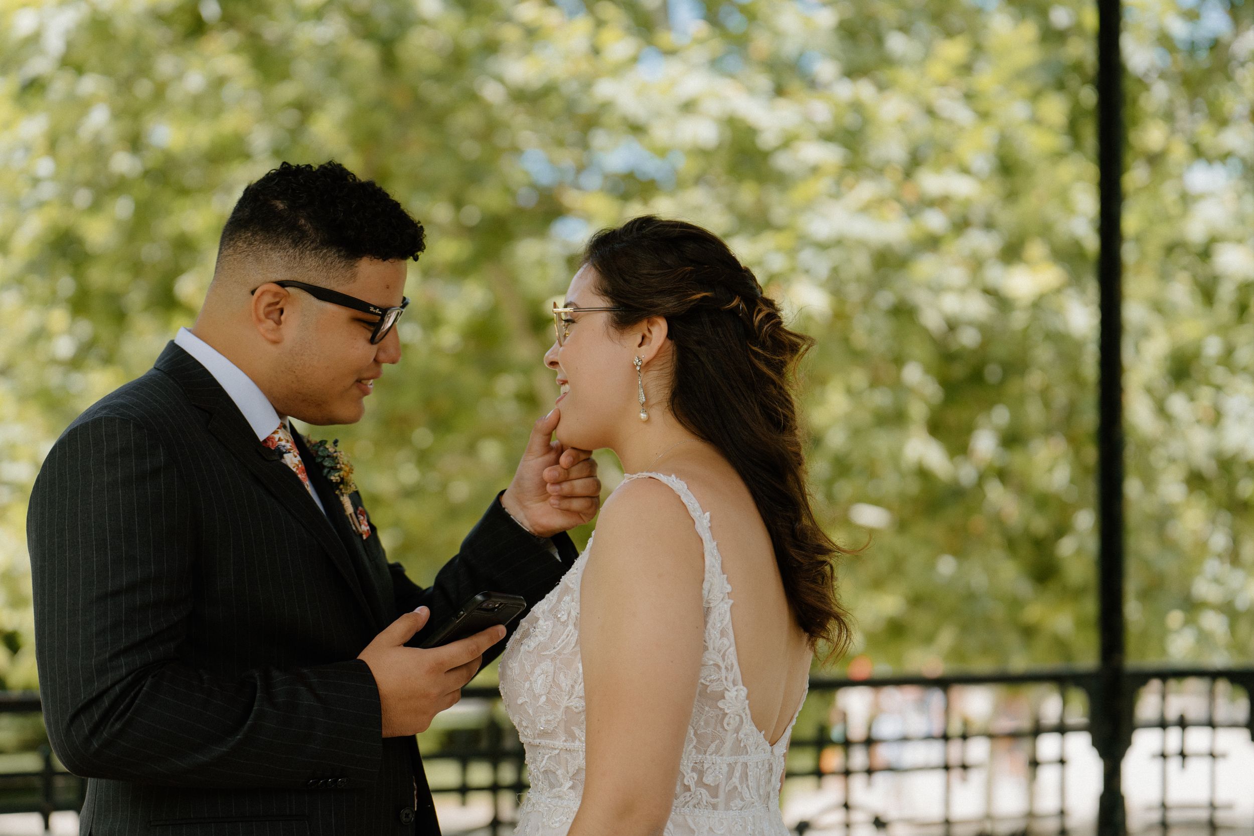 A couple shares an emotional moment while reading their vows during an outdoor wedding ceremony.