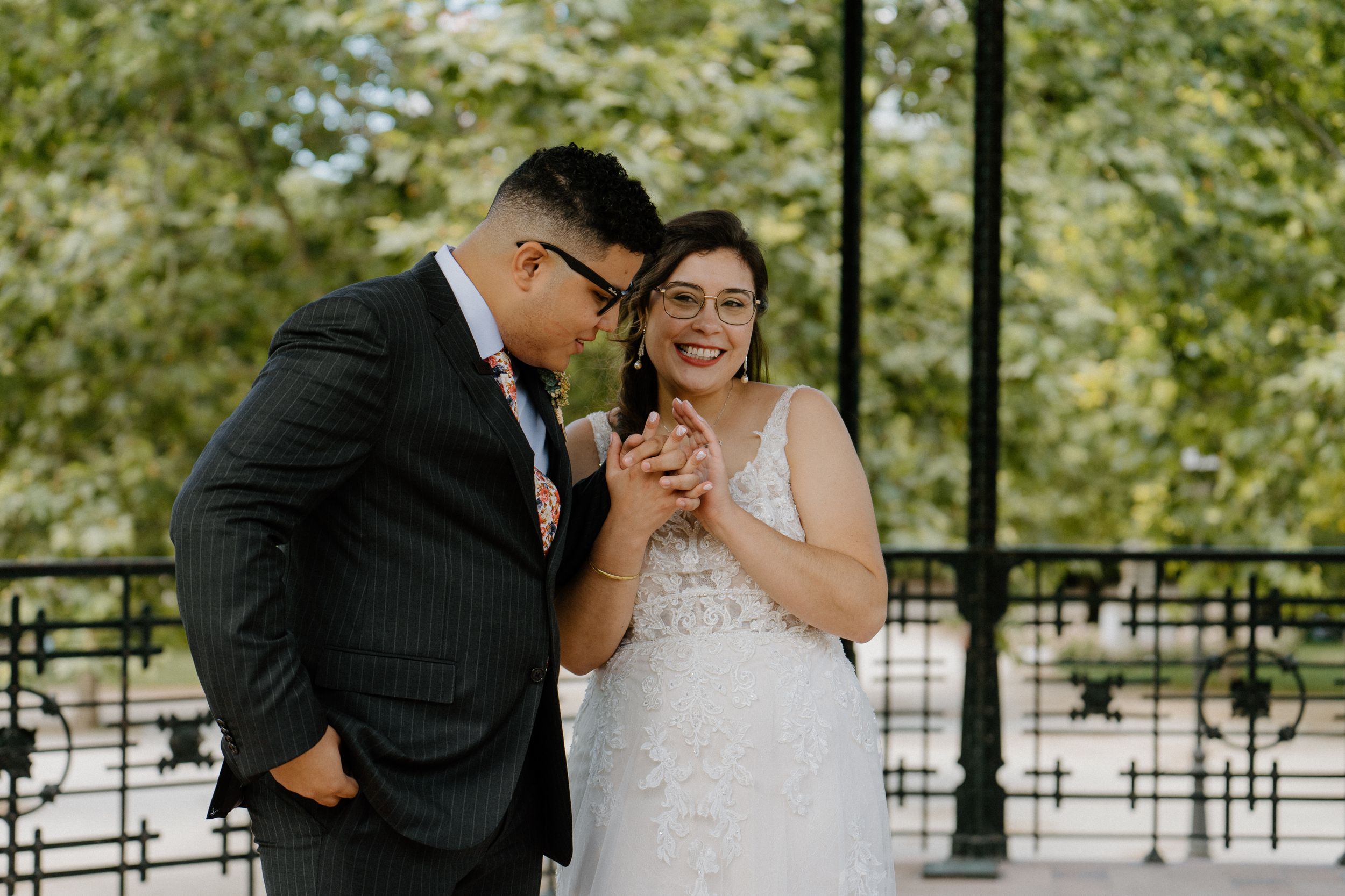 A couple laughs joyfully together during their wedding photoshoot in a park setting.