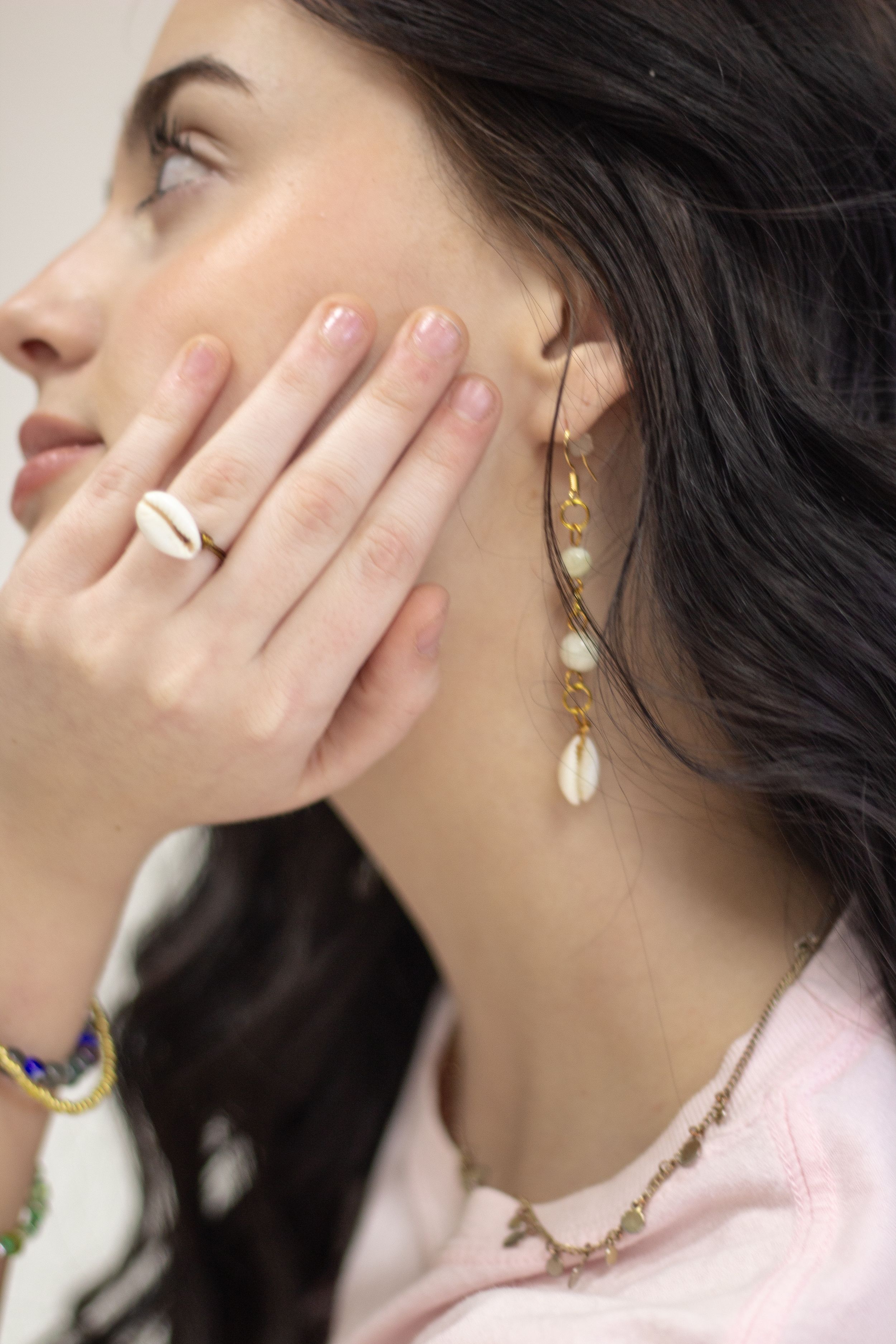 Close-up view of delicate gold jewelry including rings and earrings worn with a pink top.