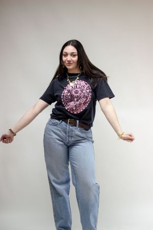 A person wearing a black t-shirt with pink graphics poses in a  against a light background during a company branding photoshoot.
