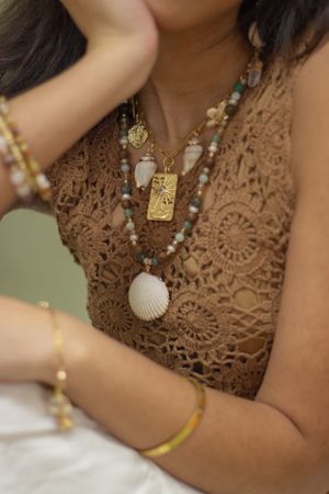 Close-up view of delicate gold jewelry including rings and earrings worn with a brown top during a photoshoot.