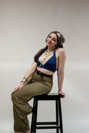 A fashion model wearing a navy blue crop top and olive green pants poses on a black stool against a light backdrop during a branding shoot.