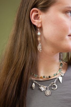 Close-up view of delicate gold jewelry including rings and earrings worn with a grey top during a photoshoot.