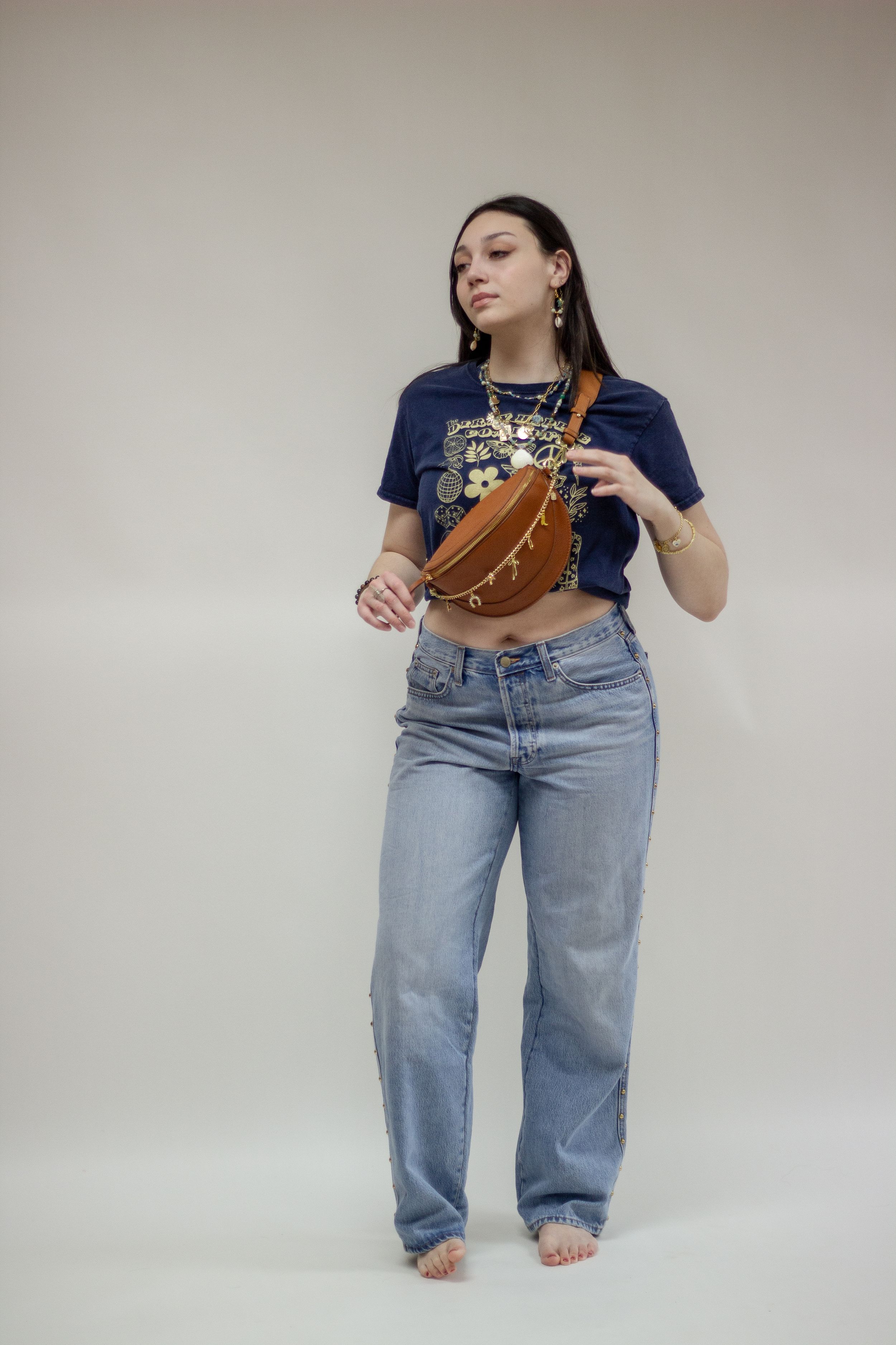 A fashion model wearing a navy blue crop top and jean pants poses on a black stool against a light backdrop during a branding shoot.