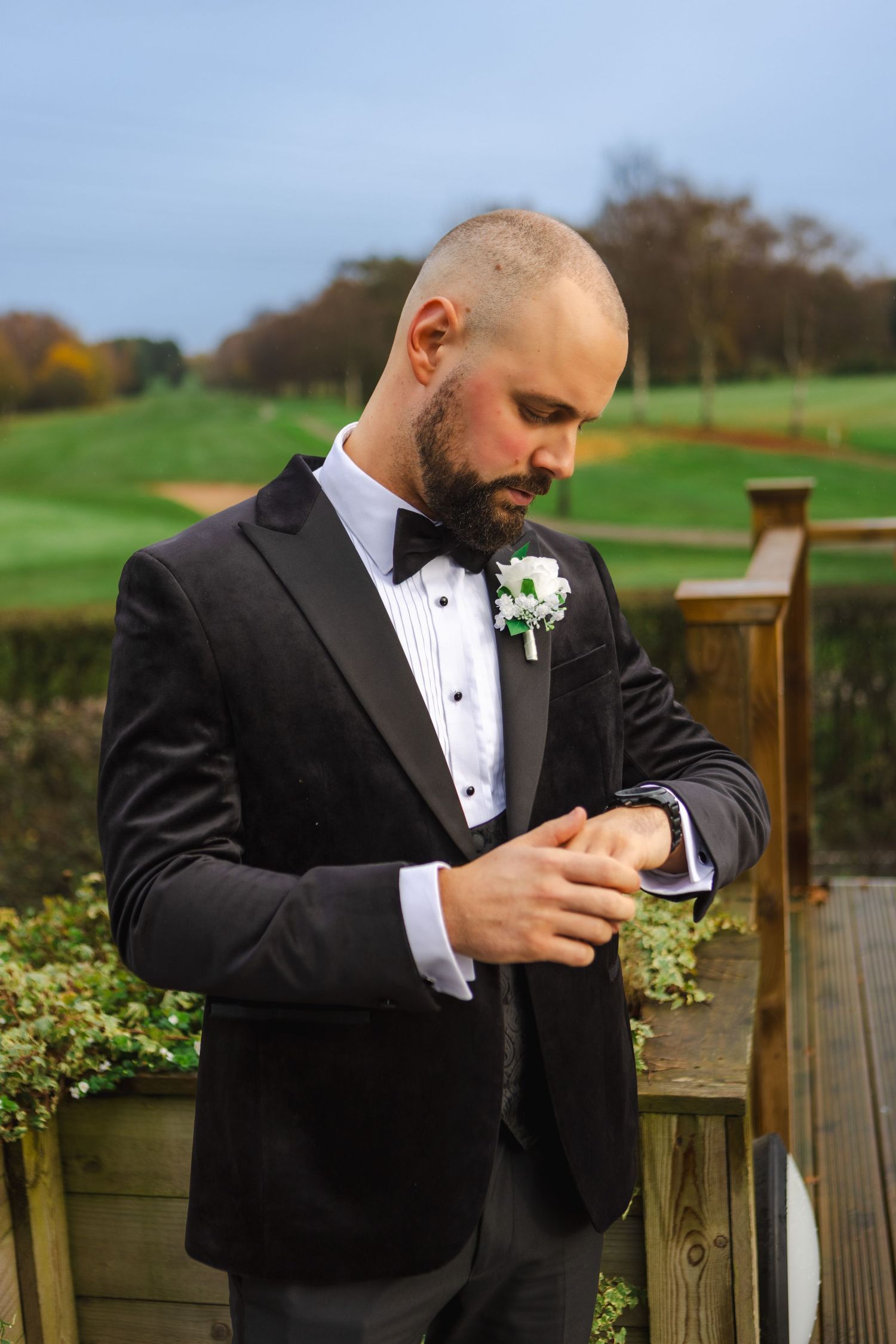 Groom in black tuxedo checking a small box outdoors.