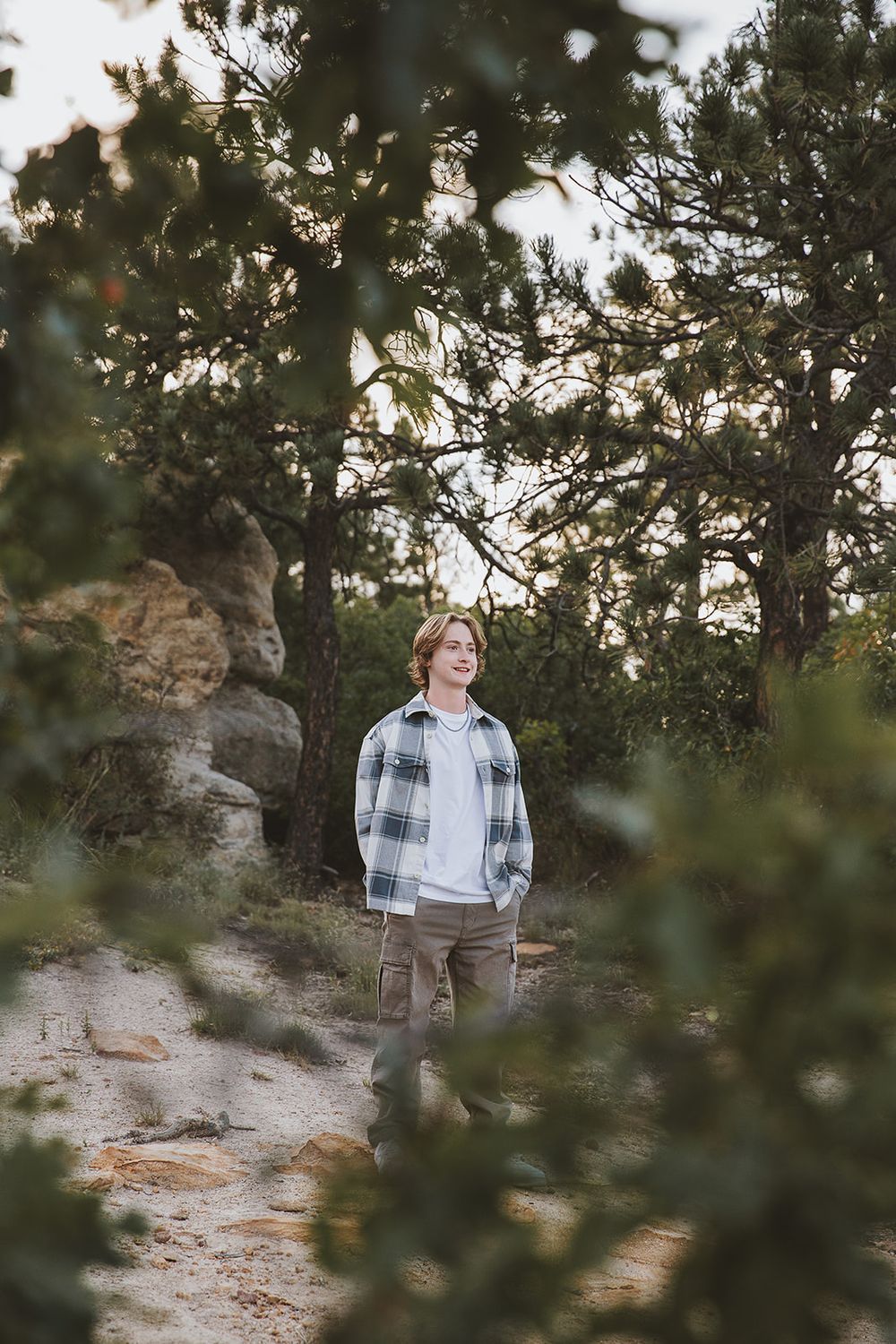 Figure framed by pine trees against rocky landscape.