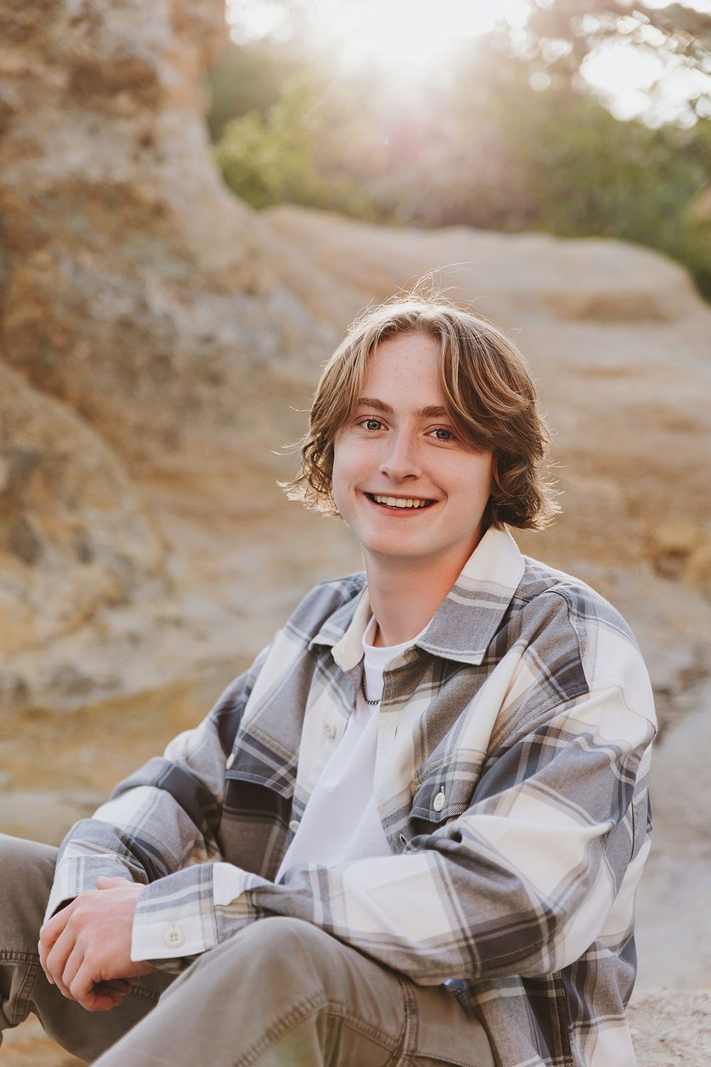 Outdoor portrait against rock formations wearing grey plaid jacket and white collar shirt.