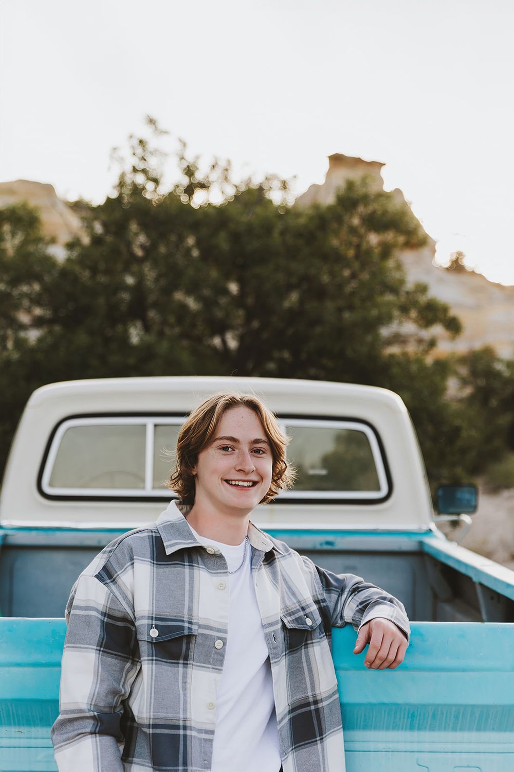 A casual portrait in front of a vintage blue pickup truck wearing a plaid flannel jacket and white shirt.