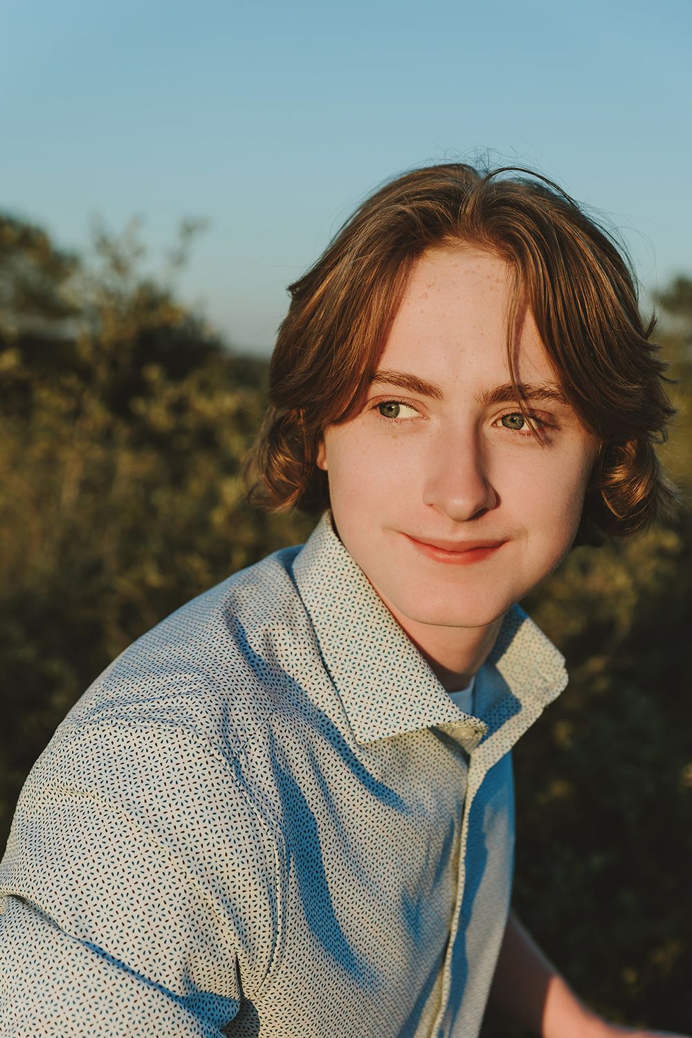 Warm sunset portrait with gentle smile wearing dotted button-down shirt.