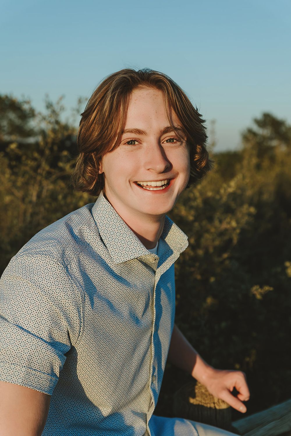 Close-up outdoor portrait in patterned blue shirt against natural foliage.