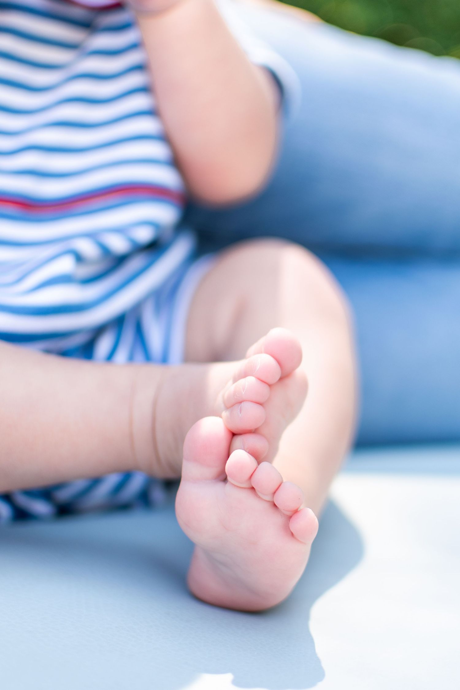 Close-up of a baby's tiny bare foot against a blue surface with a striped shirt visible in the background.