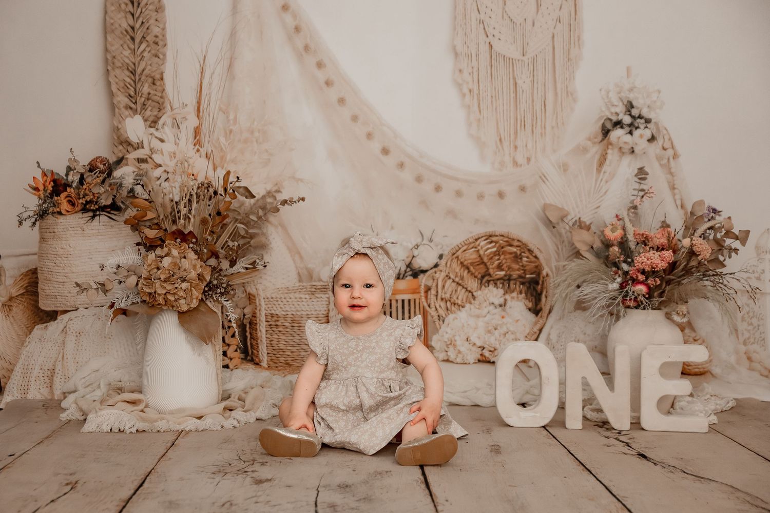 First birthday celebration setup with beige decor, floral arrangements and large ONE letters in rustic boho style. bop cakesmash photography