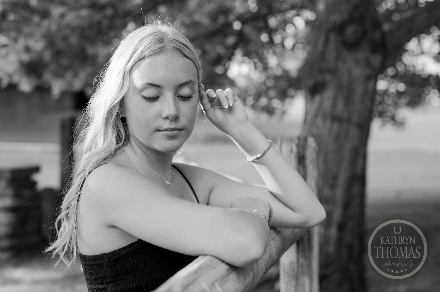 A black and white portrait of a woman leaning against a fence in a contemplative pose.