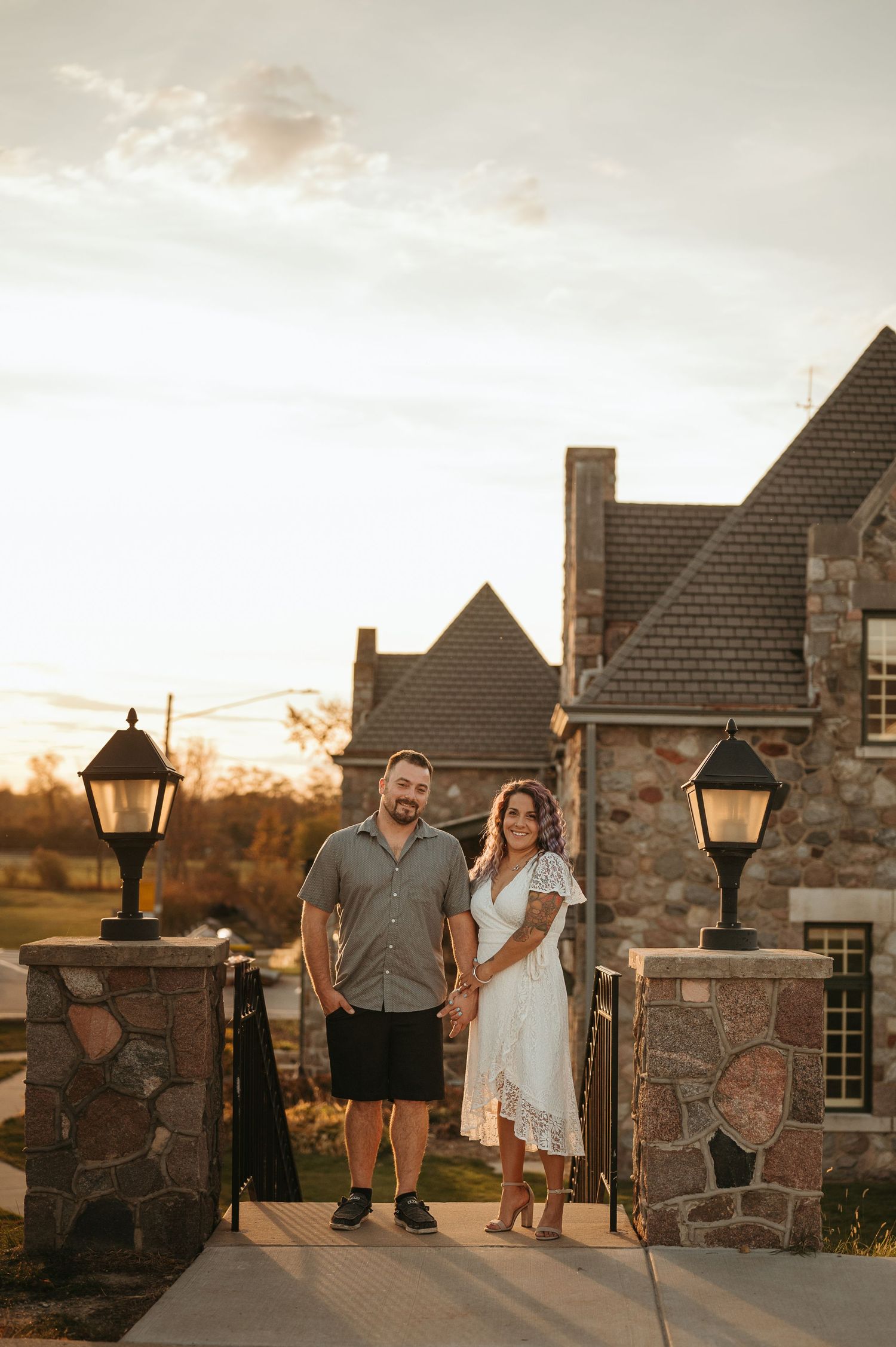 Couple standing on stone steps of rustic house during golden hour sunset.