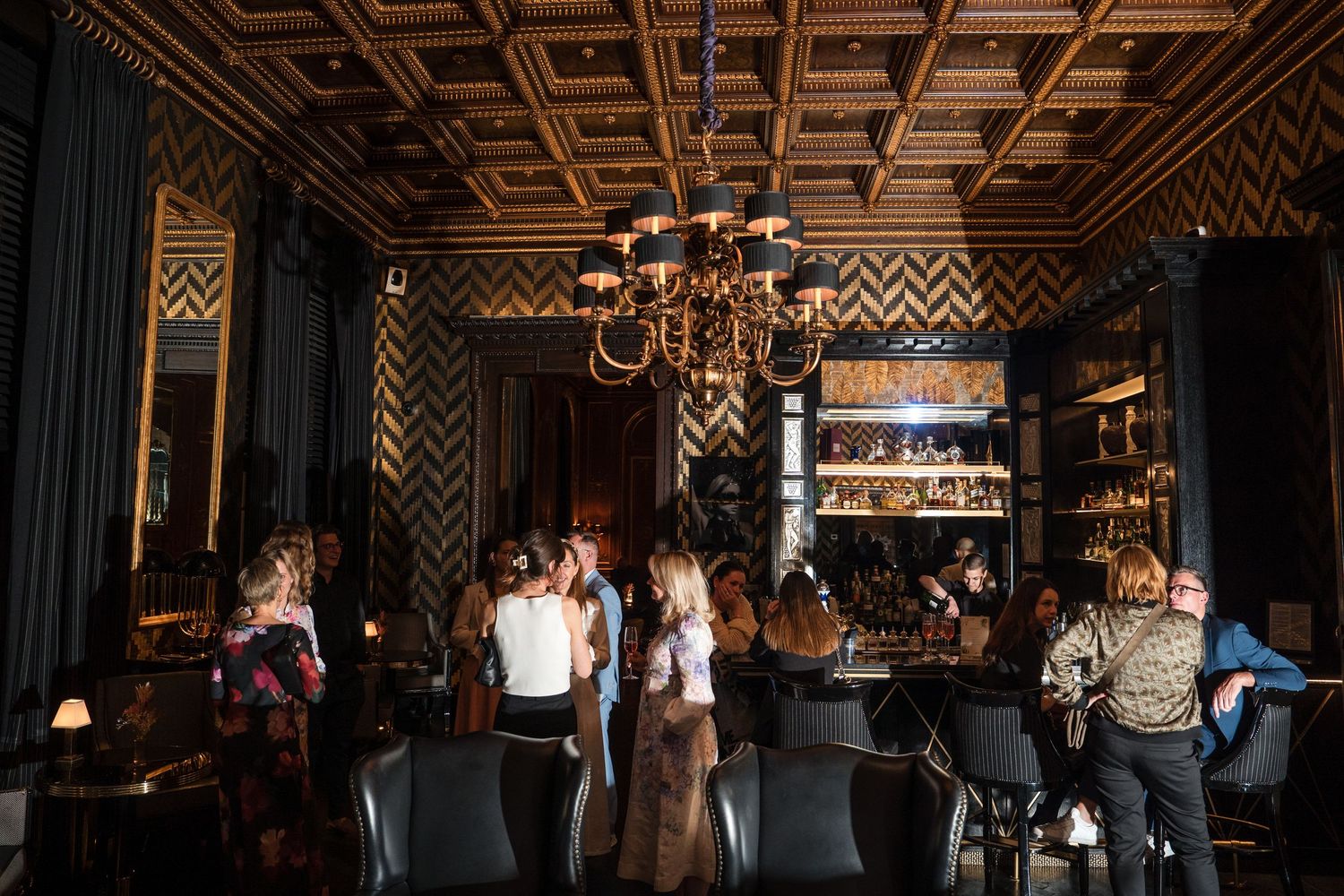 People gather inside a dimly lit restaurant with geometric patterned walls and warm ambient lighting.