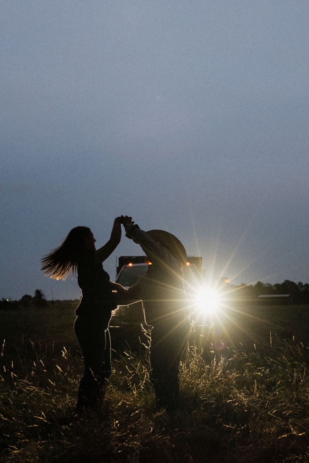 Silhouettes of people dancing in a field at sunset with sun rays creating dramatic backlighting effects.