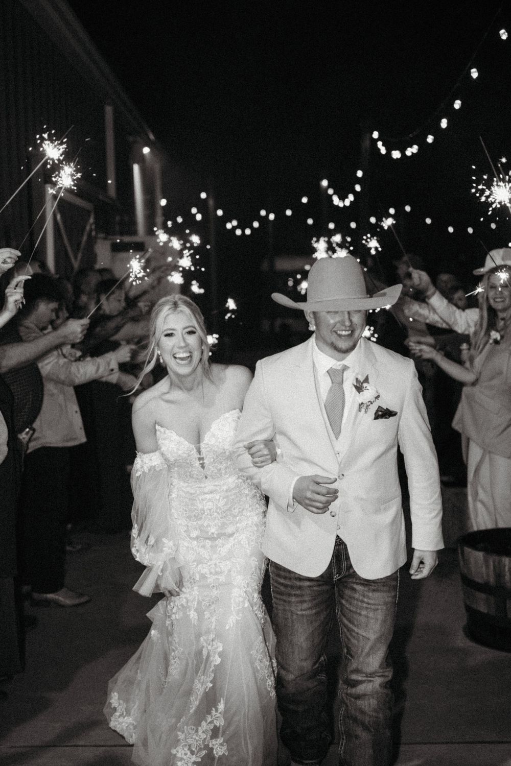 A couple dancing and celebrating at a nighttime wedding reception with sparklers and guests in the background.