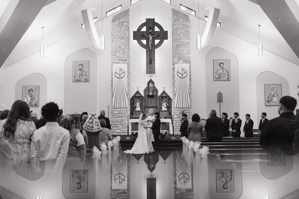 A black and white photo of a church wedding ceremony with guests seated in pews and a Celtic cross above the altar.