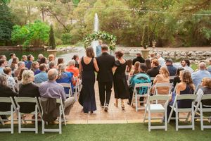 Outdoor wedding ceremony setup with white chairs arranged in rows on grass surrounded by lush trees and greenery.